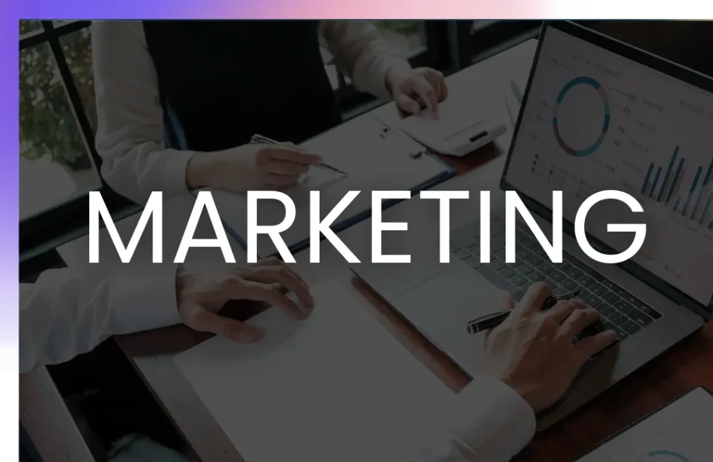 Two people working at a desk with a laptop displaying charts and graphs, overlaid with the word "MARKETING" in bold white letters.