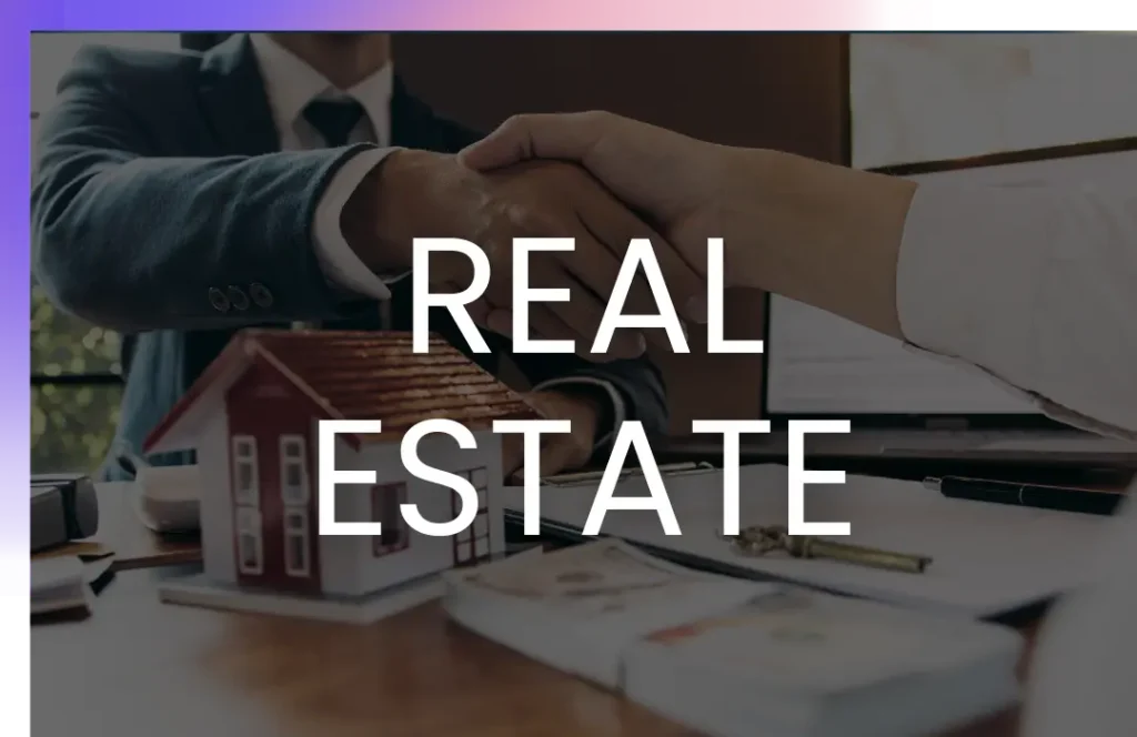 Two people shaking hands over a desk with a small house model and documents, overlaid with the words "REAL ESTATE" in bold white letters.