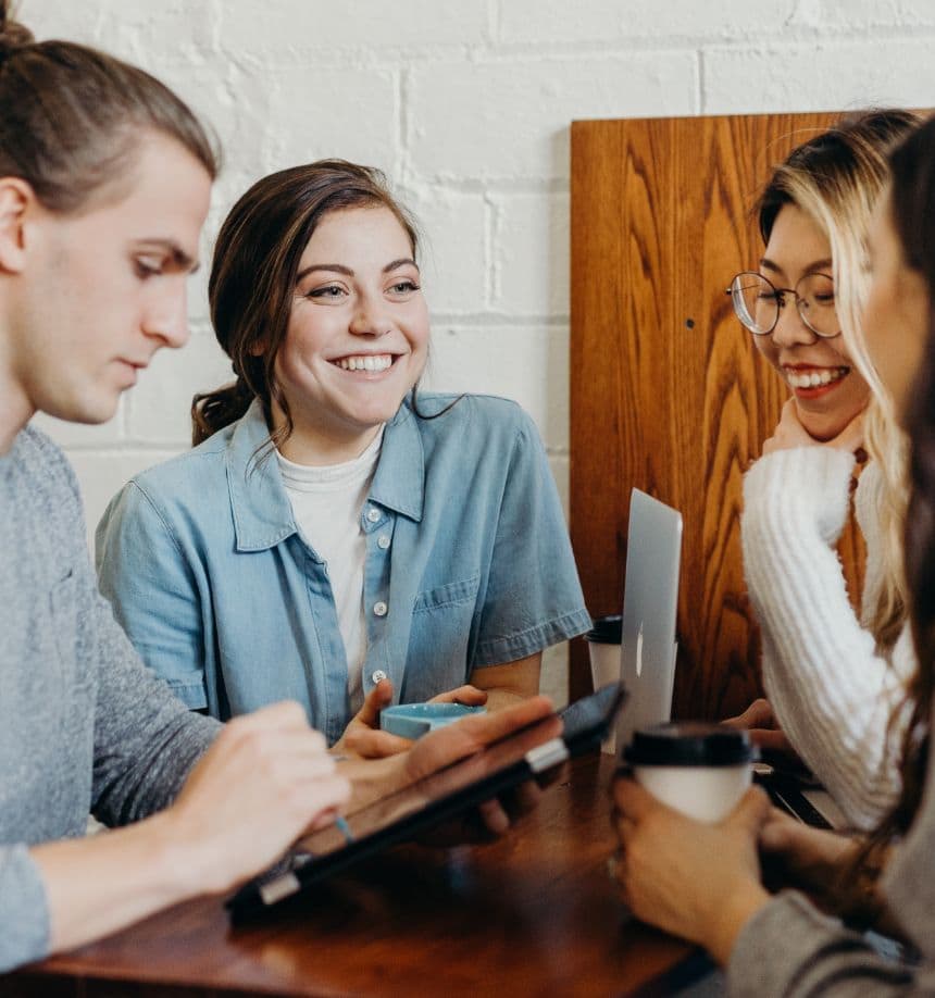 Three young professionals engage in a lively discussion, smiling and collaborating around a table with a laptop and coffee cups.